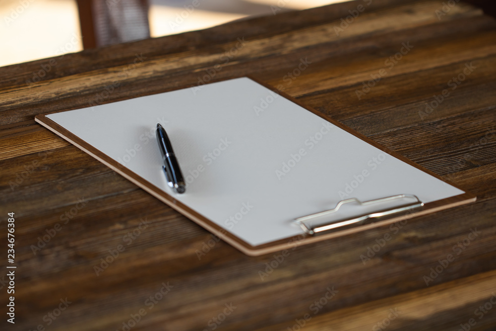 Clipboard with white sheet on wood background. Top view.Vintage style.