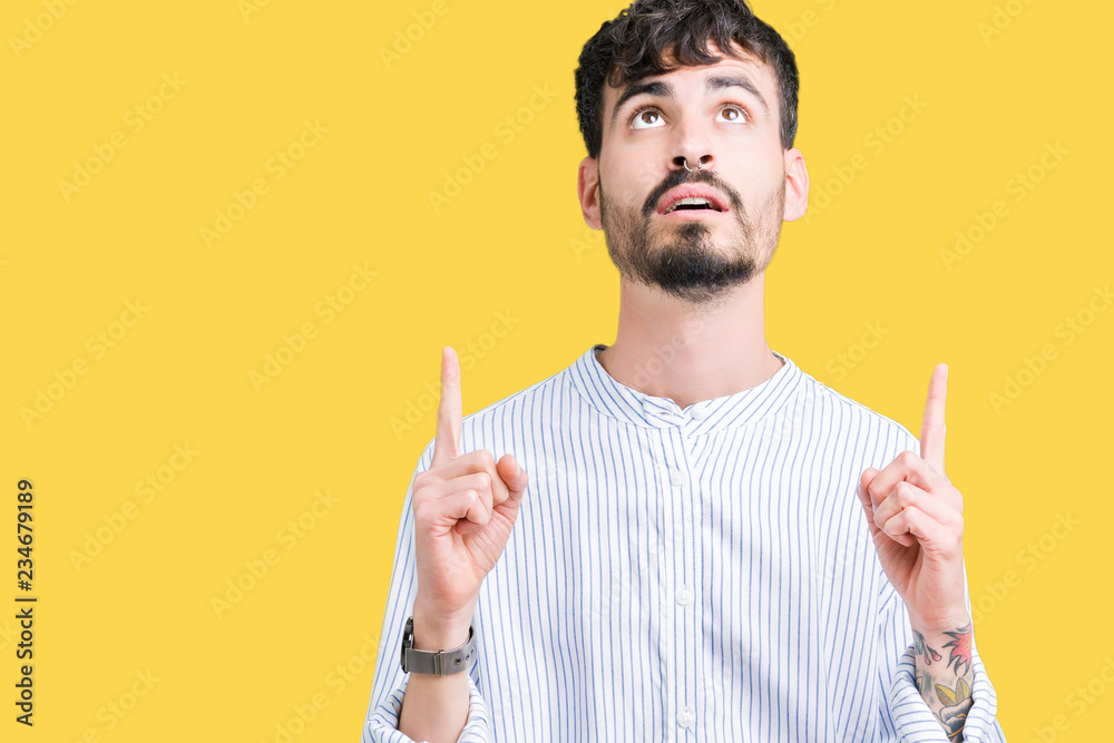 Young handsome business man over isolated background amazed and surprised looking up and pointing with fingers and raised arms.