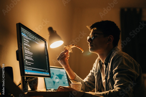 young programmer having pizza snack wile working late night at his home
