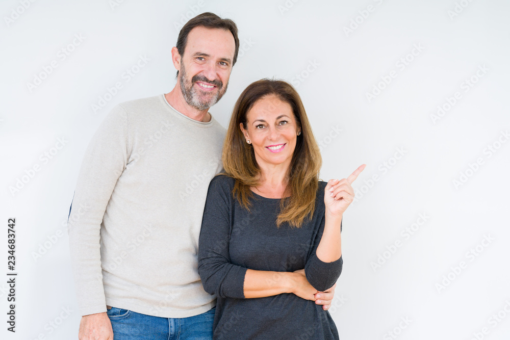 Beautiful middle age couple in love over isolated background with a big smile on face, pointing with hand and finger to the side looking at the camera. Beautiful middle age couple in love over isolated background with a big smile on face, pointing with hand and finger to the side looking at the camera.
