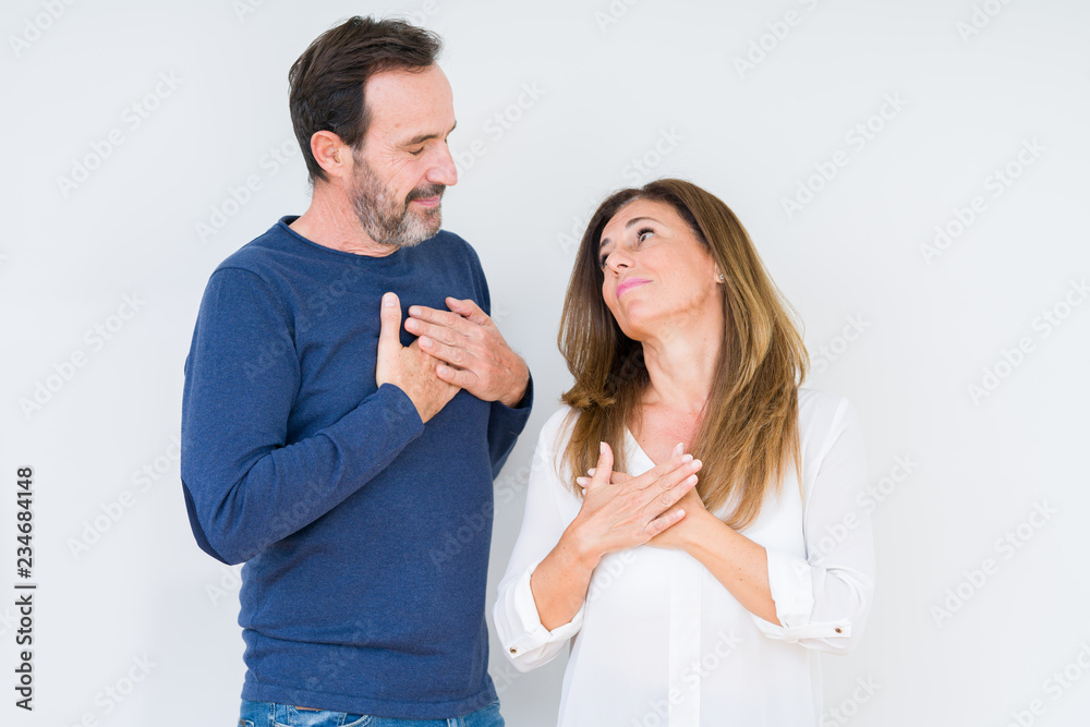 Beautiful middle age couple in love over isolated background smiling with hands on chest with closed eyes and grateful gesture on face. Health concept. Beautiful middle age couple in love over isolated background smiling with hands on chest with closed eyes and grateful gesture on face. Health concept.