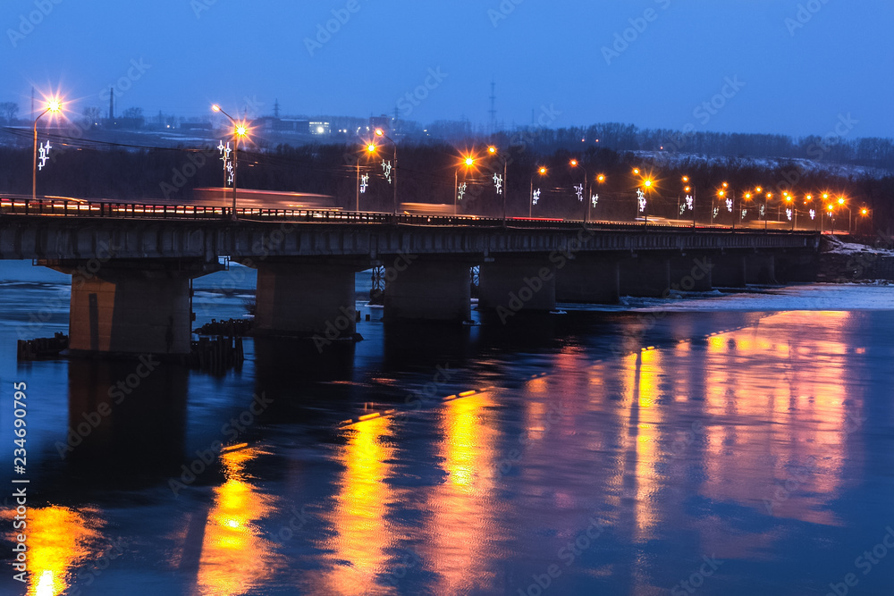 Large concrete bridge over the river, illuminated by street lamps.