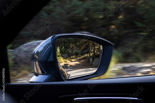 Rural road reflected in the mirror glass of a car parked on the shoulder 