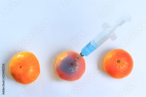 Added mandarin with a syringe. The background is white but not isolate, in the syringe is blue liquid. Chemical experiments in the food industry