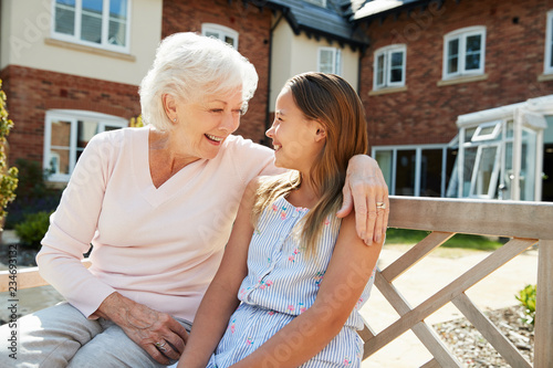 Granddaughter Sitting On Bench With Grandmother During Visit To Retirement Home