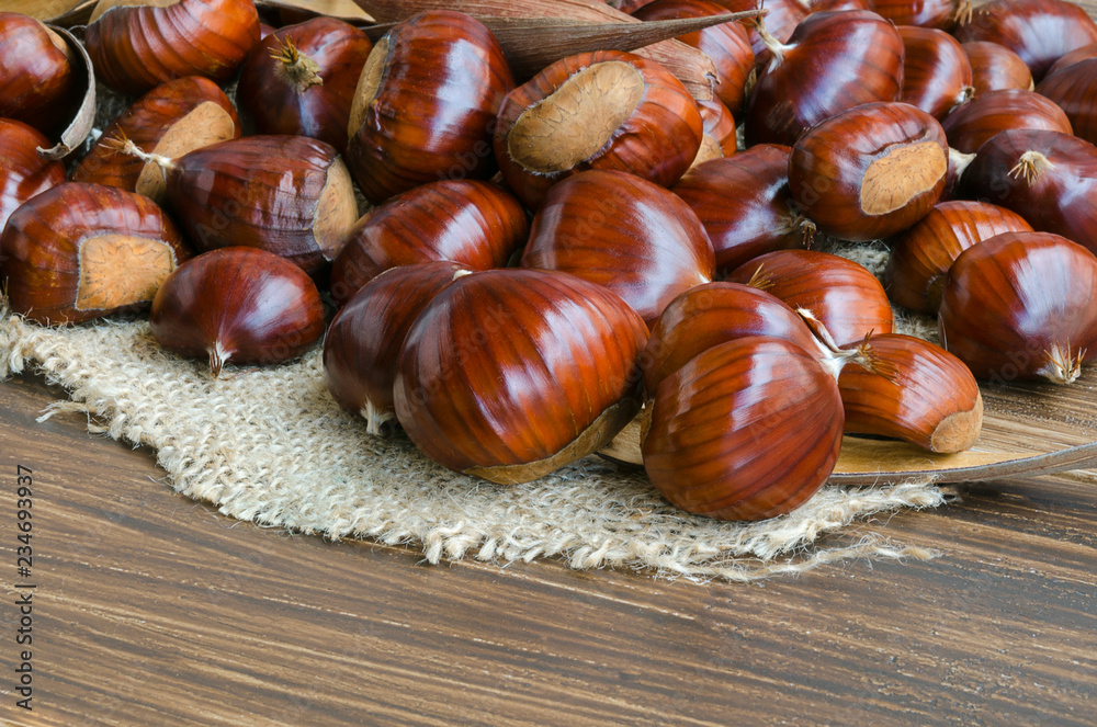 Obraz premium Heap of big tasty chestnuts on wooden table.Perfect food for vegeterian. Close up.