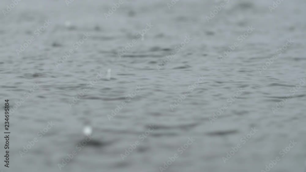Eye level, extreme closeup of raindrops falling on grey lake surface. Good audio of rain. Shallow depth of field. Eye level, extreme closeup of raindrops falling on grey lake surface. Good audio of rain. Shallow depth of field.