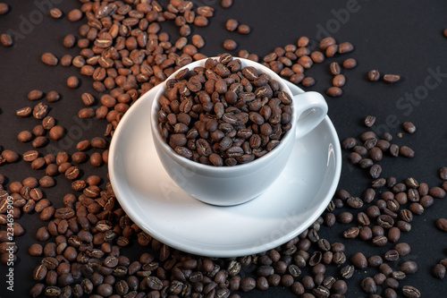 Close up of coffee cup in coffee beans on black background.