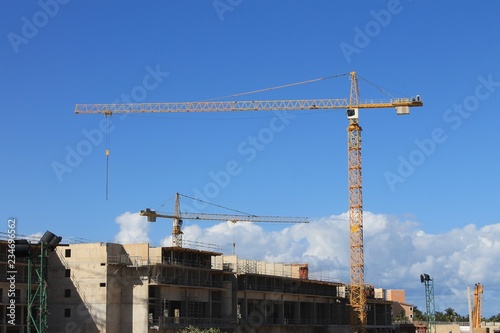 Cranes working on a building construction project, Varadero, Cuba. Two yellow cranes, cement structure. Blue sky with some light cloud on the horizon.