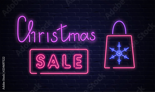 Christmas sale pink neon promo poster with shopping bag on brick textured background.