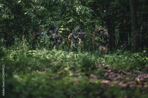 Camouflaged soldiers in forest during summer on patrol 