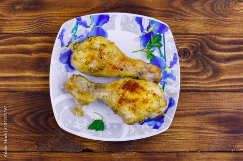 Baked chicken drumsticks with potatoes in a plate on wooden table