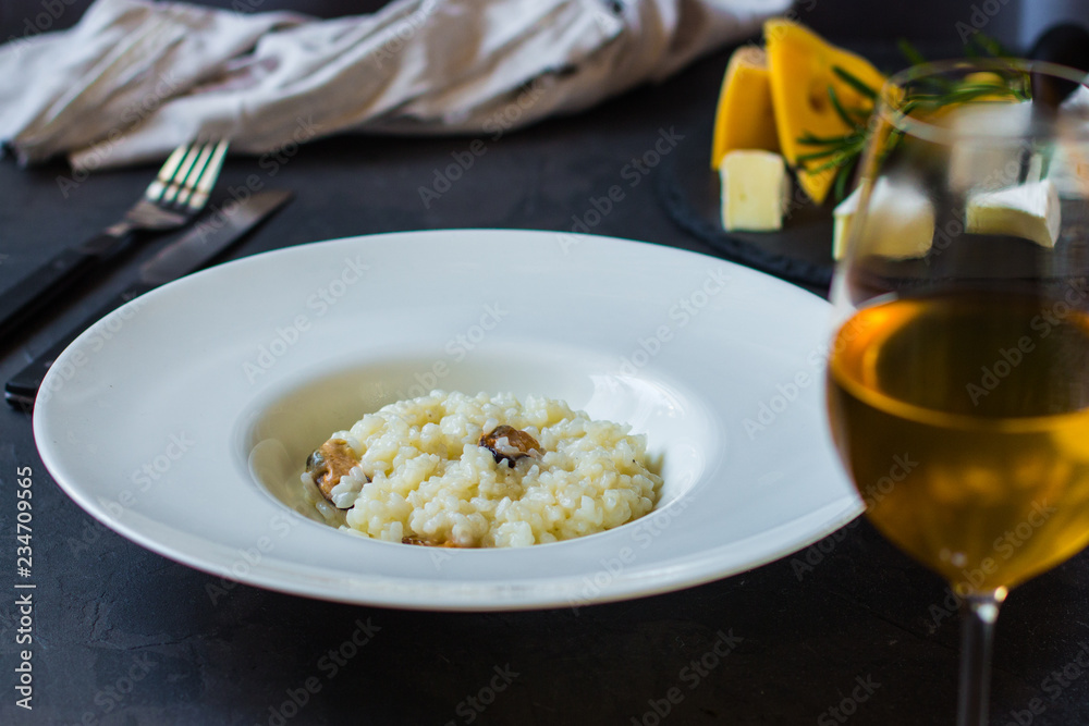 risotto with mussels (seafood rice) in a white plate and a glass of white wine on a dark background risotto with mussels (seafood rice) in a white plate and a glass of white wine on a dark background