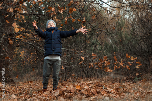 A pile of autumn, yellow foliage, a child, a boy playing with foliage in a park, throws up leaves. Concept autumn, yellow leaves, autumn mood. Copy space. © Aliaksandr Marko