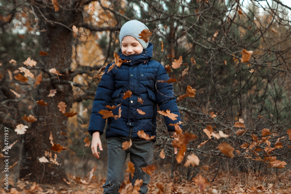 A pile of autumn, yellow foliage, a child, a boy playing with foliage in a park, throws up leaves. Concept autumn, yellow leaves, autumn mood. Copy space.