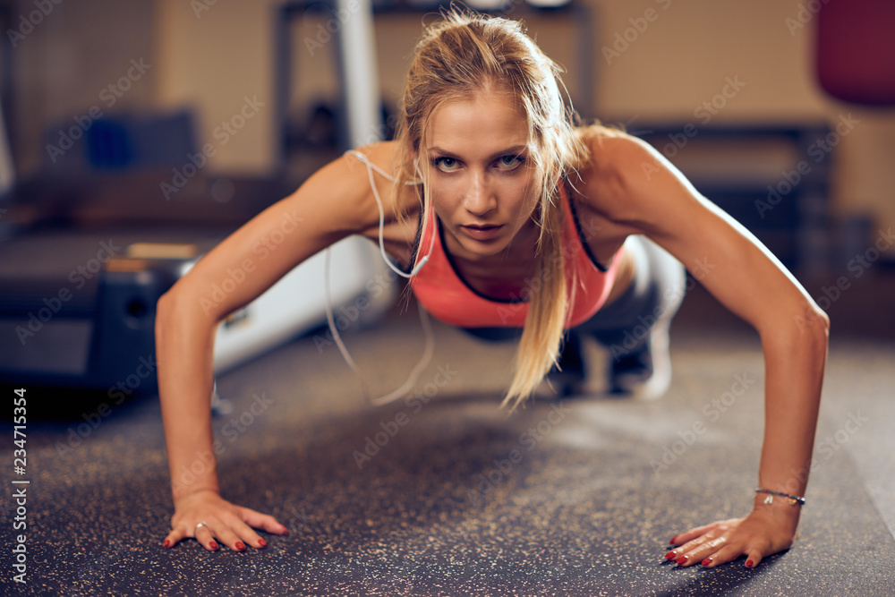 Sporty woman doing push-ups on the floor. In background exercise equipment. Gym interior. Sporty woman doing push-ups on the floor. In background exercise equipment. Gym interior.