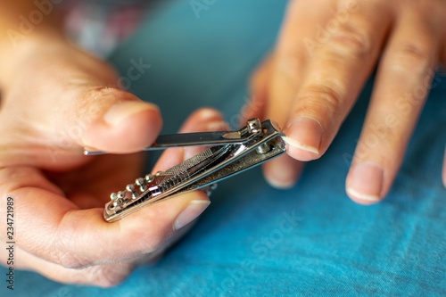 A person is cutting his nail with clipper on a blue fabric.
