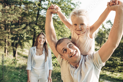 Young Adult Couple with Their Little Daughter Having Fun in the Park Outside the City, Family Weekend Picnic Concept, Three People Enjoying Summer Time © Romvy