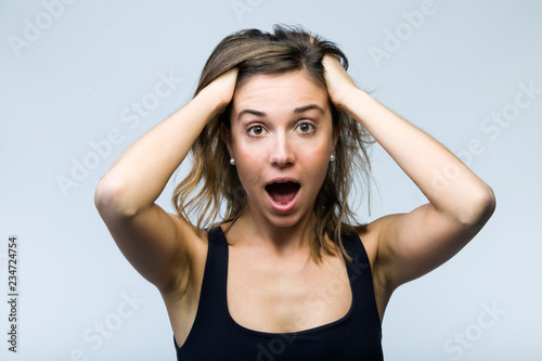 Surprised young woman screaming and putting her hands on her head looking at camera isolated on white.