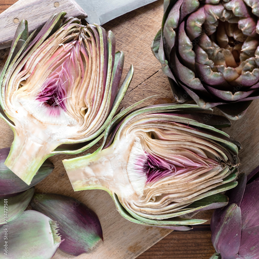 Obraz premium carciofi violetti interi e tagliati su tagliere di legno e coltello