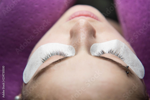 Eye lash extension procedure. Young beautiful woman eye with long false eye lashes. Close up macro shot of master making eyelashes in beauty salon.