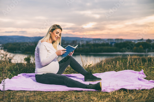 Beautiful pregnant woman enjoys reading book outdoor.