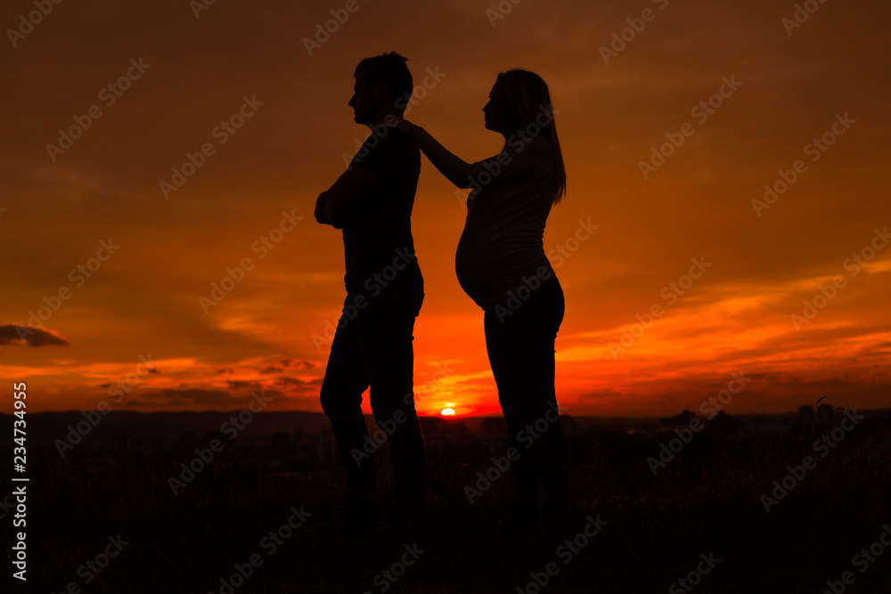 Silhouettes of angry husband and  pregnant wife while they standing outdoor.