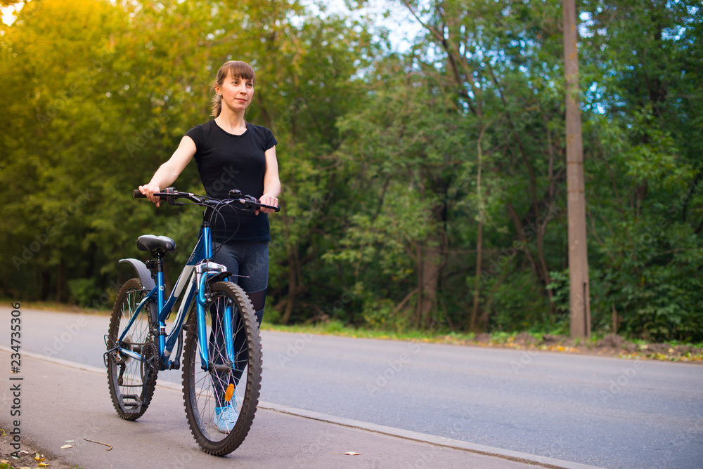 young beautiful girl leads the bike on the sidewalk