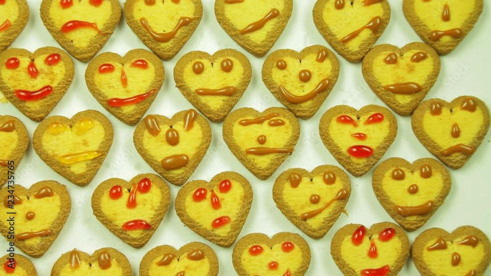 A woman is laying a cookie with a pattern of painted emoticons with icing on a white dish A woman is laying a cookie with a pattern of painted emoticons with icing on a white dish