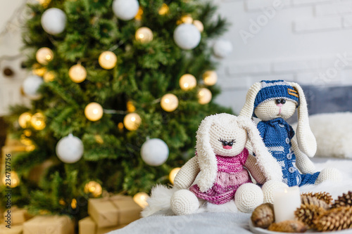 Handmade knitted rabbit. Christmas Bunny in a scarf and hat with a large pumpon among the decorative Christmas trees and balls. Christmas composition photo