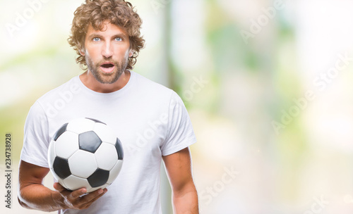 Handsome hispanic man model holding soccer football ball over isolated background scared in shock with a surprise face, afraid and excited with fear expression © Krakenimages.com