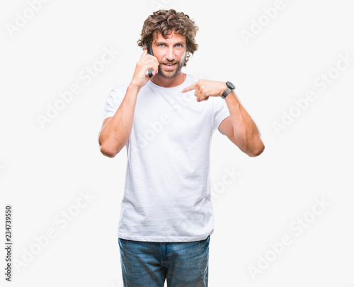 Handsome hispanic man model talking on smartphone over isolated background with surprise face pointing finger to himself