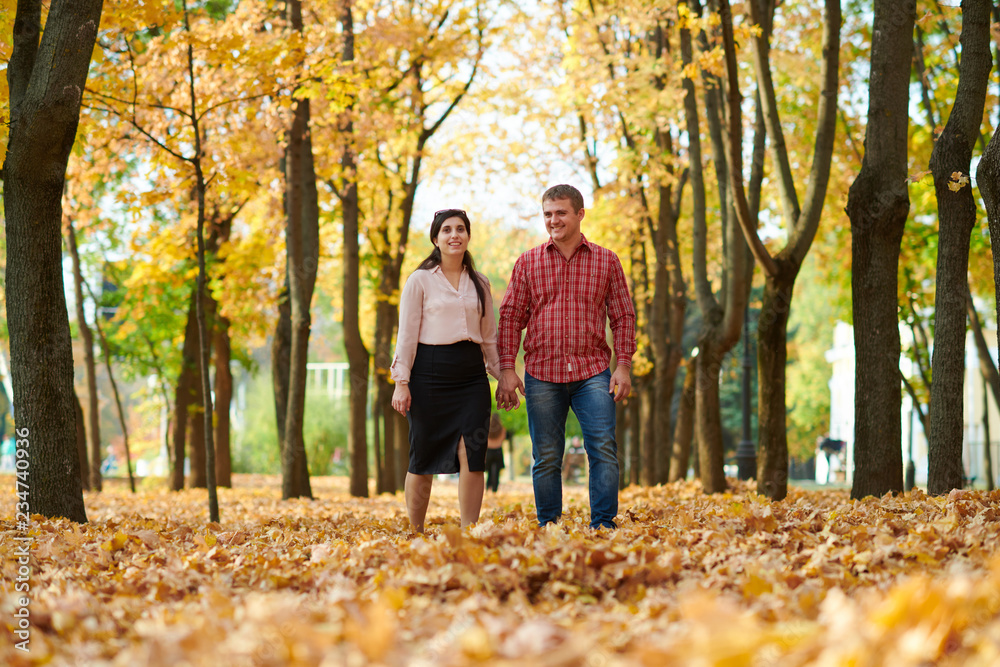 Couple is walking in autumn city park. Bright yellow trees.