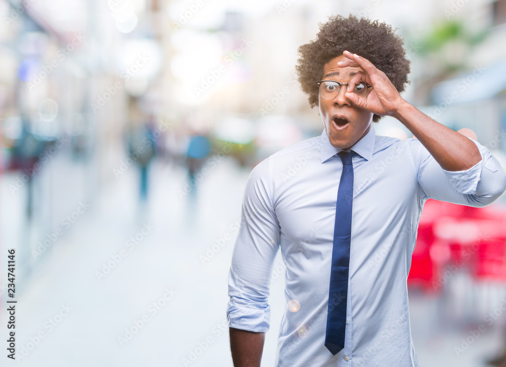 Fototapeta premium Afro american business man wearing glasses over isolated background doing ok gesture shocked with surprised face, eye looking through fingers. Unbelieving expression.