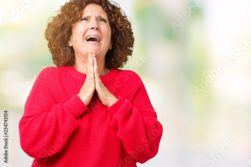 Beautiful middle ager senior woman red winter sweater over isolated background begging and praying with hands together with hope expression on face very emotional and worried. Asking for forgiveness © Krakenimages.com