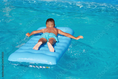 Boy lying on inflatable mattress at hotel swimming pool in summer.