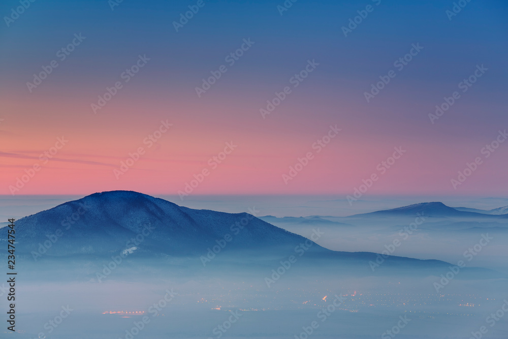 Winter scenery with sunset over the misty valleys of the Carpathians mountains, Transylvania region, Romania.