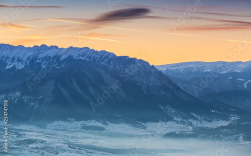 Idyllic winter landscape with snowy Piatra Craiului mountain range and misty valleys at sunset, Romania.