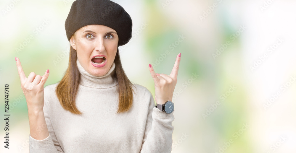 Middle age mature woman wearing winter sweater and beret over isolated background shouting with crazy expression doing rock symbol with hands up. Music star. Heavy concept. Middle age mature woman wearing winter sweater and beret over isolated background shouting with crazy expression doing rock symbol with hands up. Music star. Heavy concept.