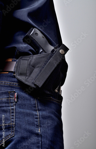 Textile holster with a pistol gun on the belt, blue jeans, a black shirt