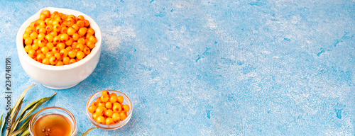 Sea-buckthorn berries in bowl and natural honey or sea buckthorn oil on blue background