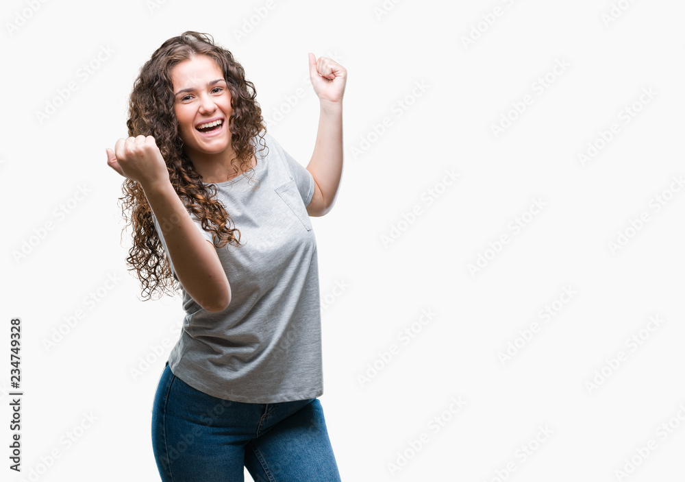 Beautiful young brunette curly hair girl wearing casual look over isolated background celebrating surprised and amazed for success with arms raised and open eyes. Winner concept. Beautiful young brunette curly hair girl wearing casual look over isolated background celebrating surprised and amazed for success with arms raised and open eyes. Winner concept.