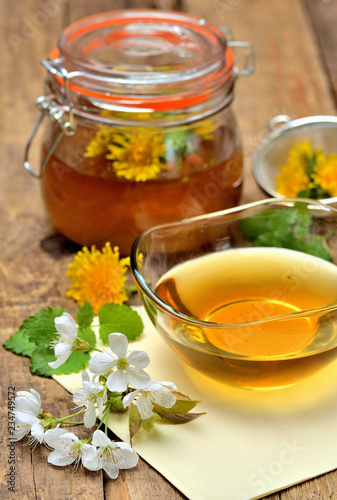 Close-up of dandelion honey, spring flowers, dandelion head around, full jar in background - vertical photo