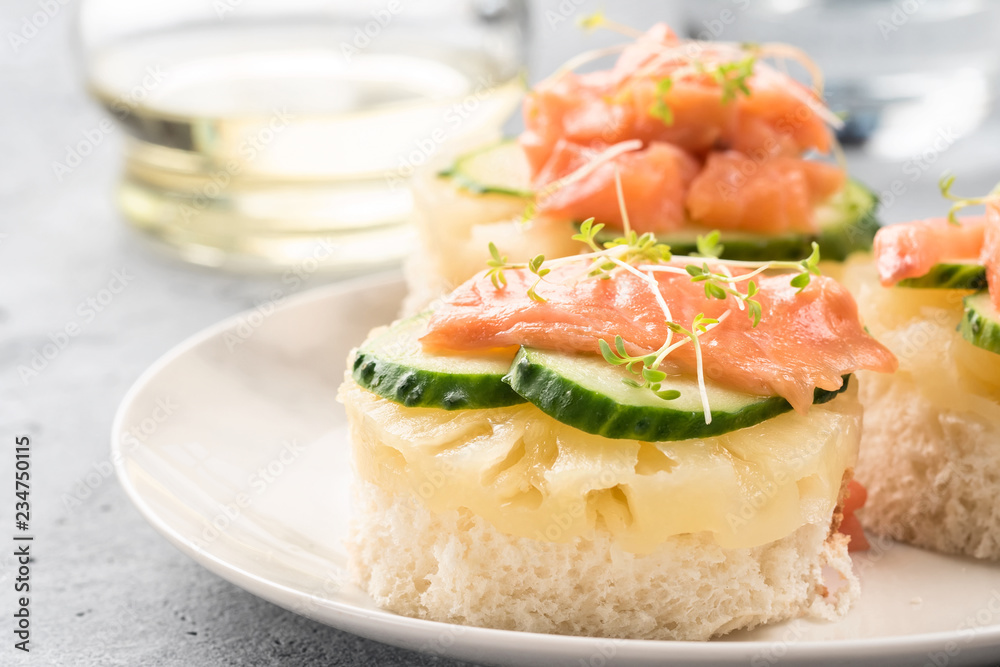 Bruschetta toast of white bread with slices of pineapple cucumber fish salmon and fresh green sprouts. Served on a white plate on table with mineral water olive oil Bruschetta toast of white bread with slices of pineapple cucumber fish salmon and fresh green sprouts. Served on a white plate on table with mineral water olive oil