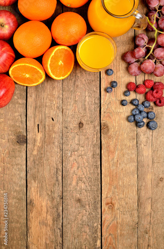 Orange juice, fresh oranges, apples, grapes, raspberries and blueberries on a wooden table - fruit background - view from above - vertical photo