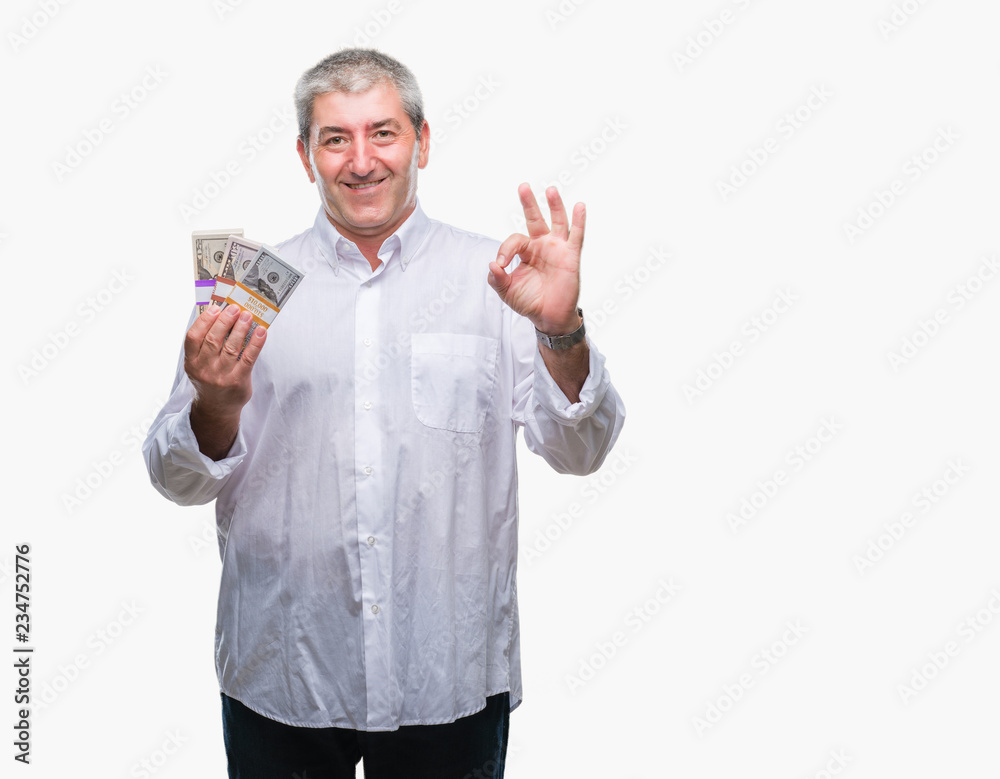 Handsome senior man holding bunch of money over isolated background doing ok sign with fingers, excellent symbol Handsome senior man holding bunch of money over isolated background doing ok sign with fingers, excellent symbol