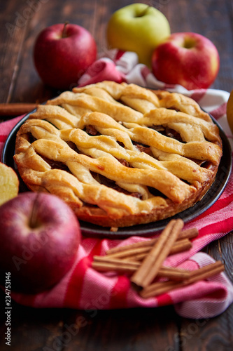 Traditional american apple pie served with fresh fruits, cinnamon sticks in a black ceramic plate. Flat lay and top view on rusty wooden table.