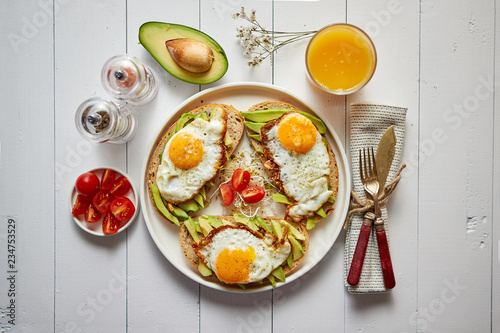 Delicious healthy breakfast with sliced avocado sandwiches with fried egg on top of bread. With orange juice, cherry tomatoes, radish sprouts, salt and peper. Flat lay, top view.