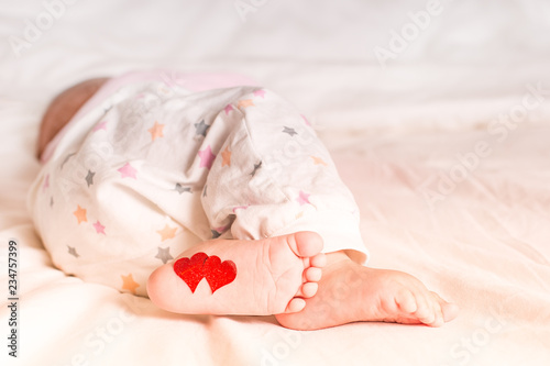 Fototapeta Naklejka Na Ścianę i Meble -  Baby foots with hearts on their feet. A newborn baby is lying on the bed.