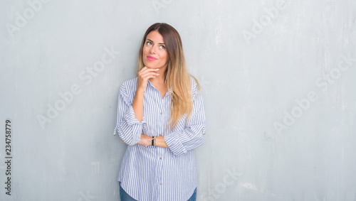 Young adult woman over grey grunge wall wearing fashion business outfit with hand on chin thinking about question, pensive expression. Smiling with thoughtful face. Doubt concept. © Krakenimages.com